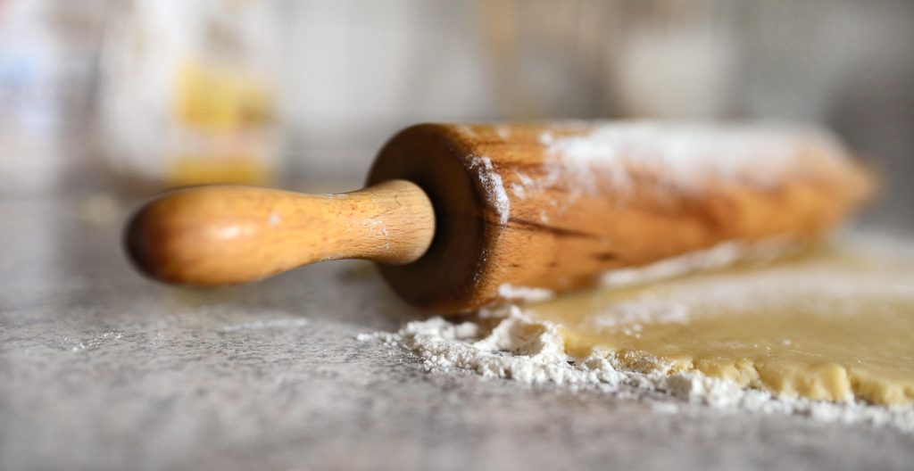 Wooden rolling pin on dough dusted with flour